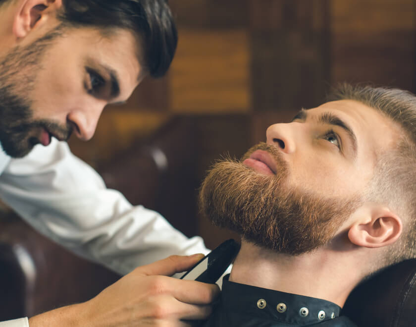 Barberare trimmar skägg på kund i barbershop